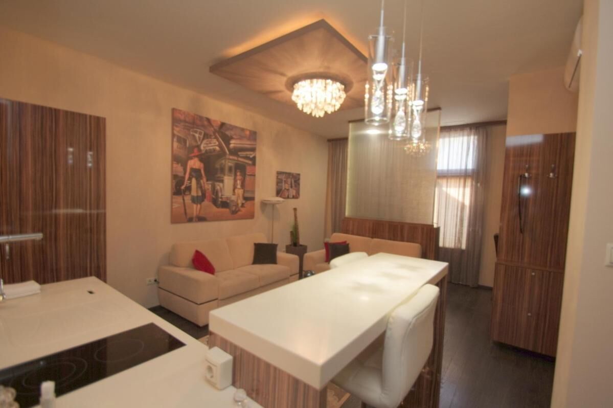 A modern hotel room with a central dining table, a sofa, a small side table, and a large painting on the wall.