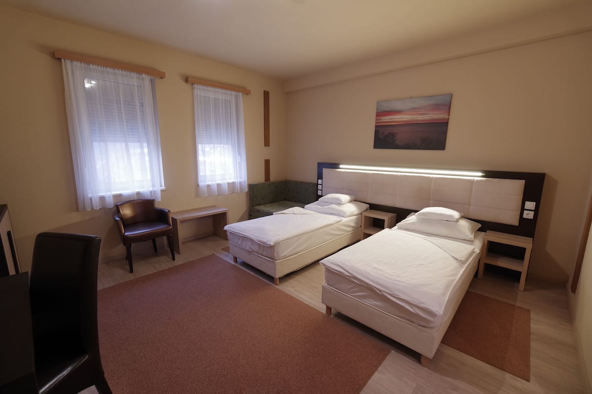 Habitación de hotel con dos camas individuales, un escritorio, una silla y un cuadro en la pared.