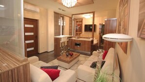 A modern living room with a wooden coffee table, white sofas, a chandelier, and a TV mounted on the wall. - Hotel Vadászkürt Superior (Szekesfehervar)