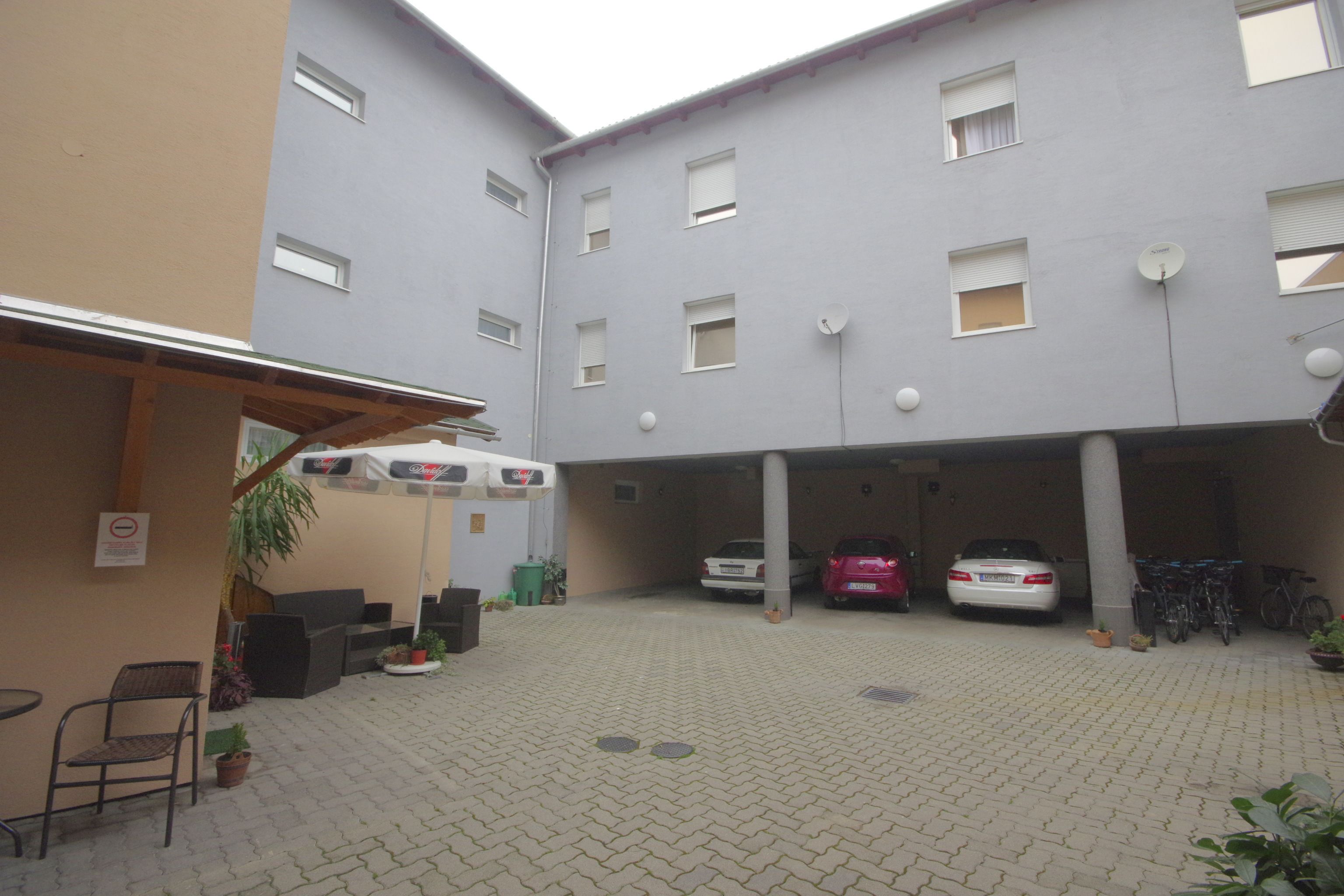 A courtyard with a covered seating area, two cars, and bicycles parked under a building with multiple windows.