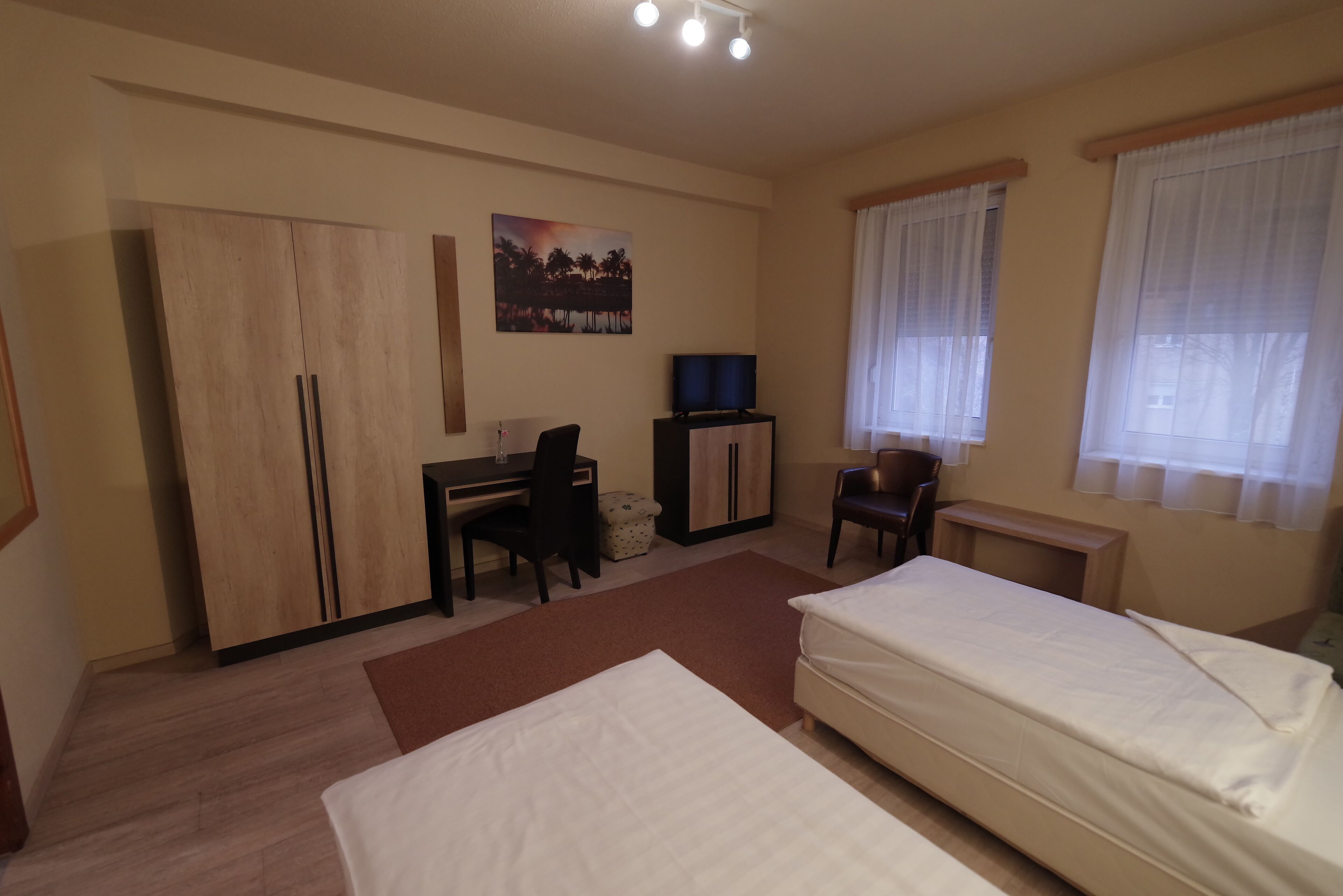 Habitación de hotel con cama, escritorio, silla, armario, televisor y ventanas.