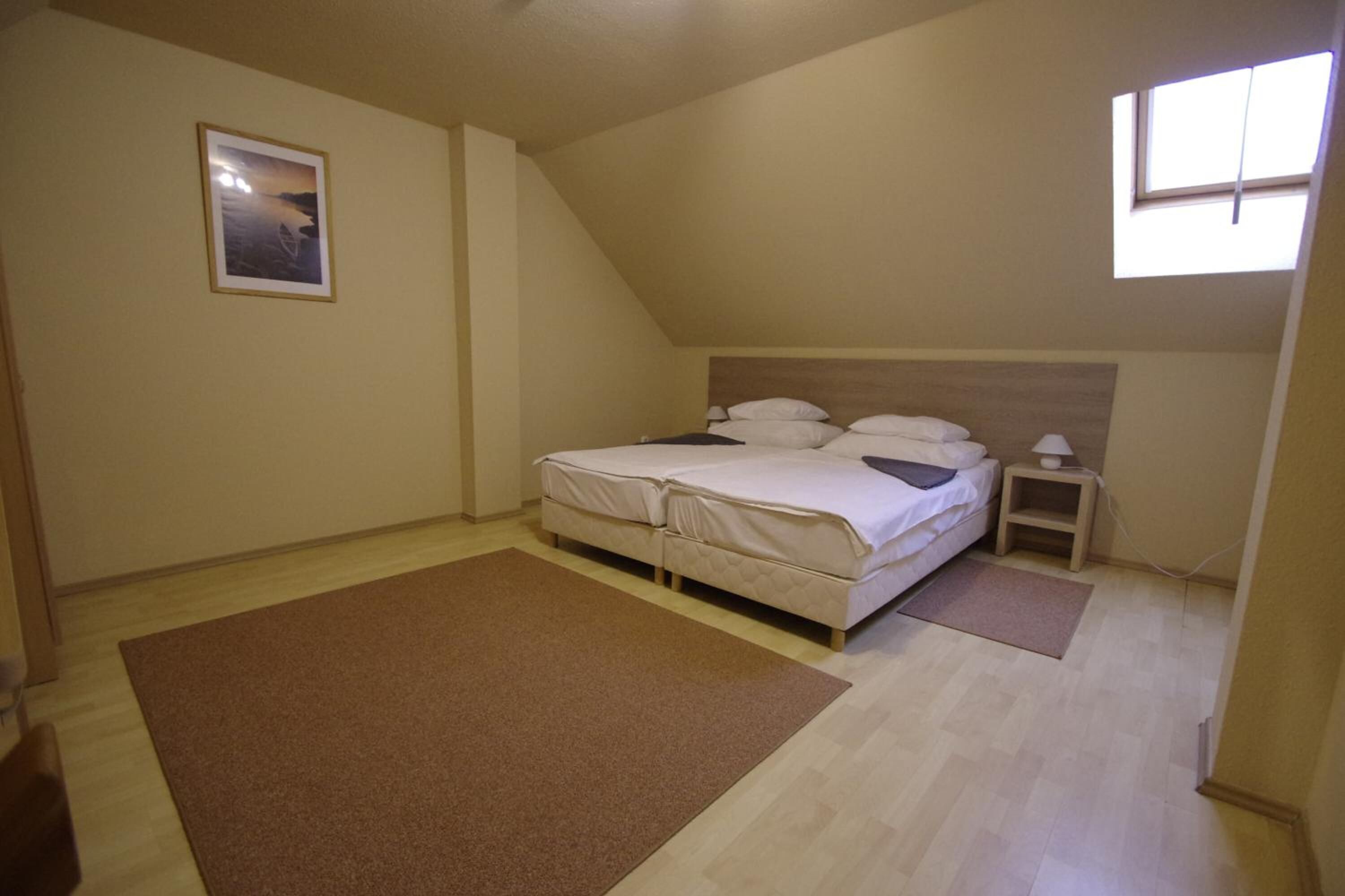 Un dormitorio con cama, mesita de noche, ventana y un cuadro en la pared.