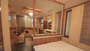 A modern hotel room with a large bed, a sitting area with a sofa and armchairs, a small desk, and a bathroom with a mirror. - Hotel Vadászkürt Superior (Szekesfehervar)