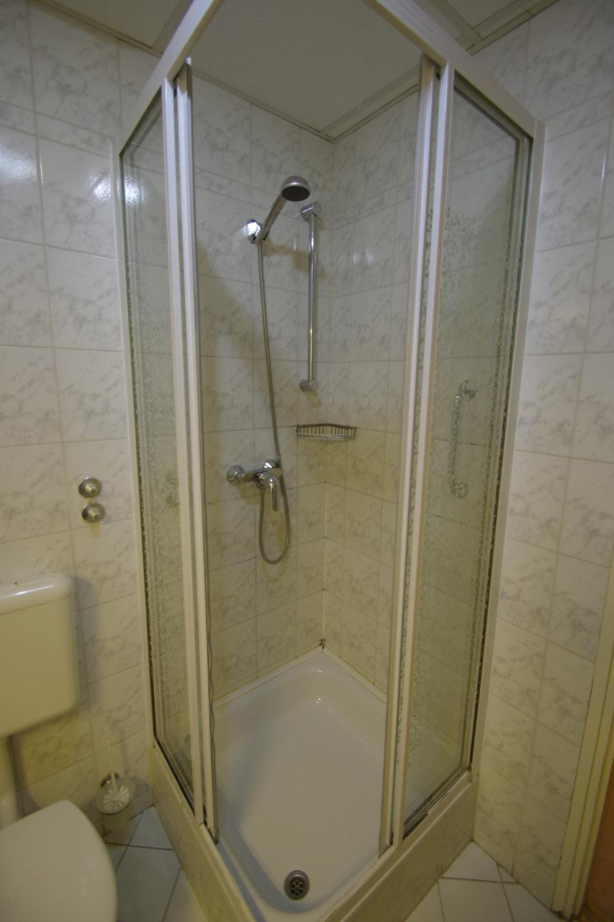 A shower with a glass door, a handheld showerhead, and a handheld showerhead.