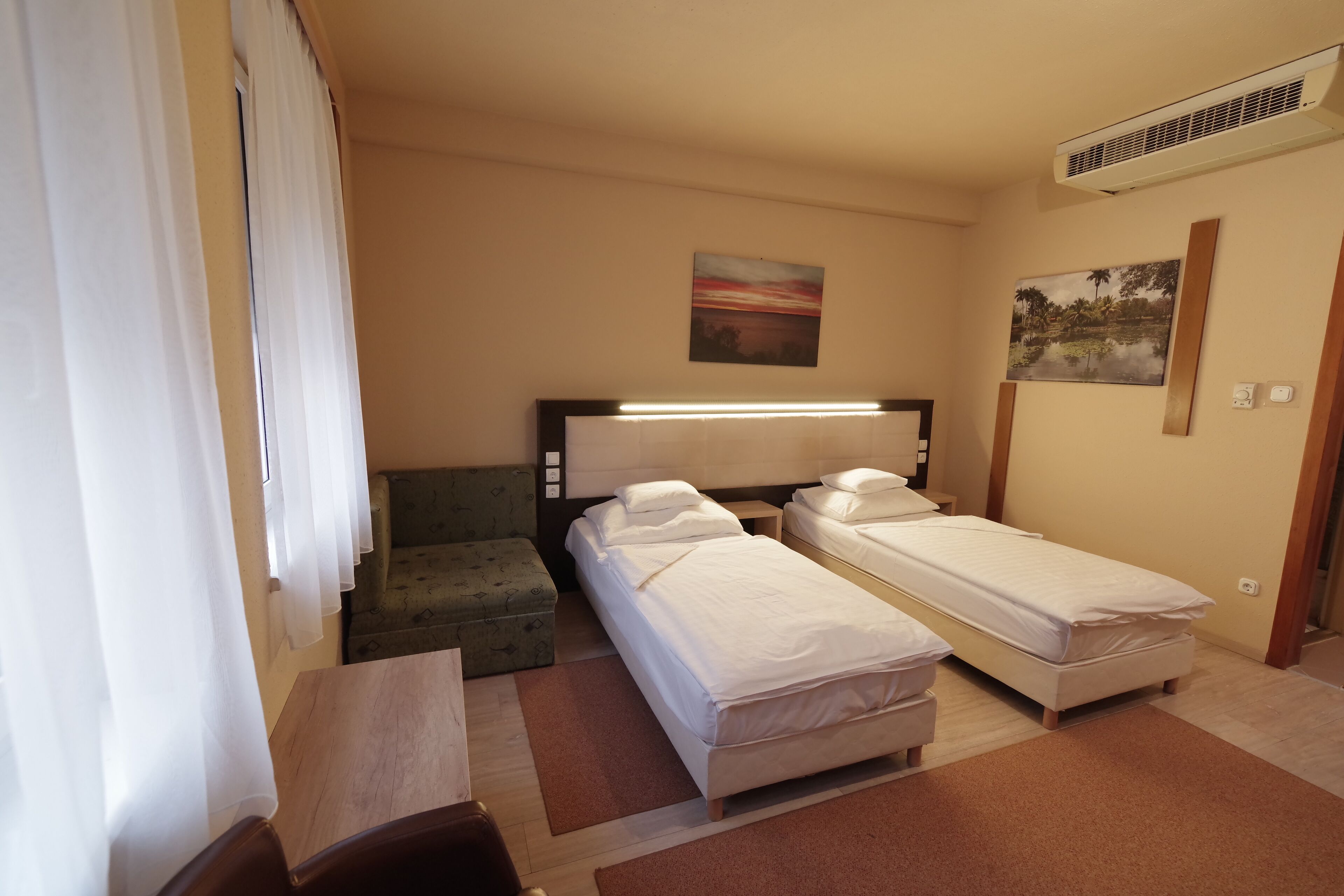 A hotel room with two single beds, a sofa, a desk, and a window with curtains.