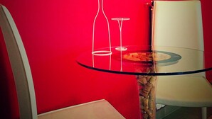 A red wall with a welcome sign in multiple languages, a glass table with a bottle and a glass, and two white chairs. - Hotel RossoVino (Milan)