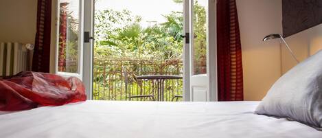 Ein Schlafzimmer mit Bett, einem Fenster mit Blick auf Grünflächen und einem Balkon.