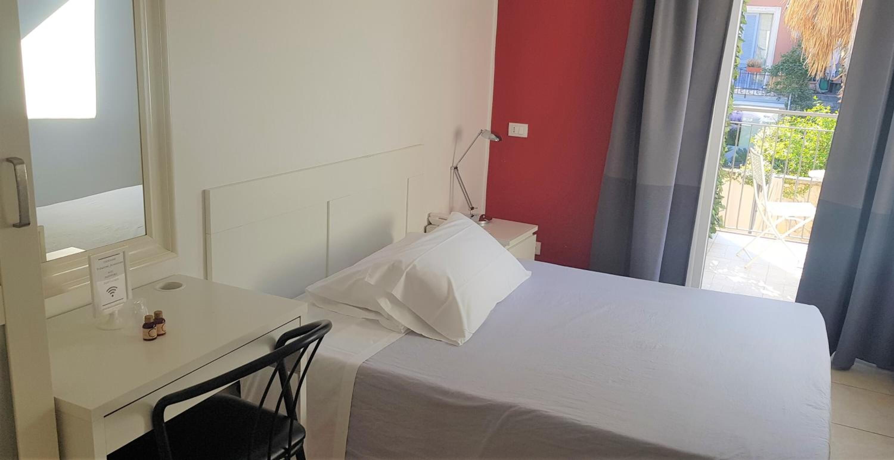 Una camera d'albergo con un letto, una scrivania e una sedia. Si vede una finestra con vista sull'esterno.