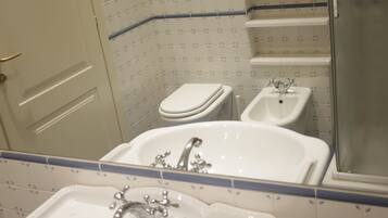 Un bagno con lavandino, bidet, WC e uno specchio che riflette l'ambiente.