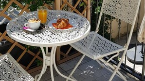 A round table with a white metal frame and a matching chair, a croissant, a glass of orange juice, and a cup of coffee. - Hotel RossoVino (Milan)