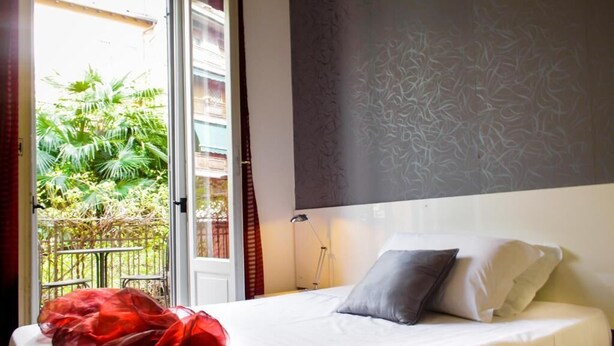 A hotel room with a bed, a nightstand, and a window with a view of greenery outside. - Hotel RossoVino (Milan)
