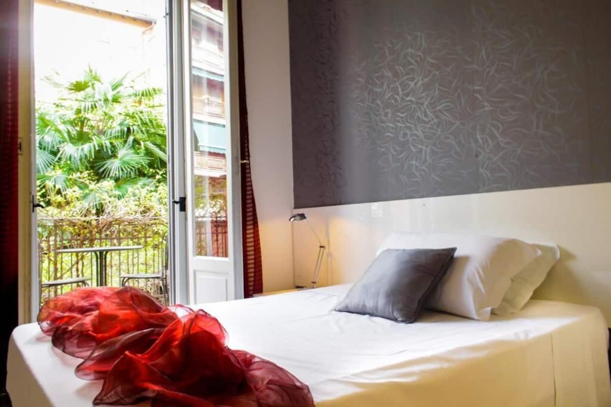 Una habitación de hotel con una cama, una mesita de noche y un ventanal con vistas a zonas verdes.