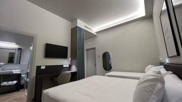 Una habitación de hotel con cama, escritorio, silla, televisor y espejo.