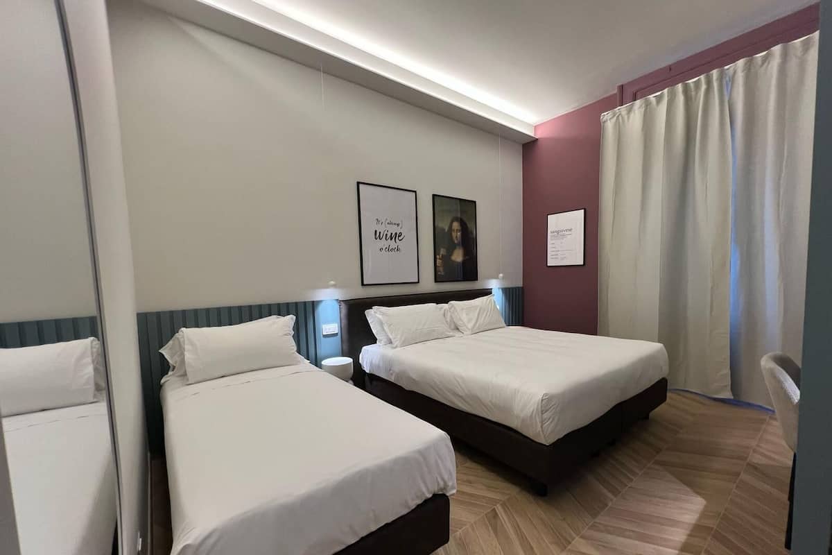 Habitación de hotel con dos camas, un espejo, un cuadro enmarcado de una mujer y una lámpara fijada a la pared.