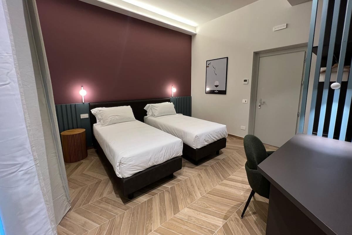 Habitación de hotel con dos camas, un escritorio, una silla, una puerta y una lámpara fijada a la pared.