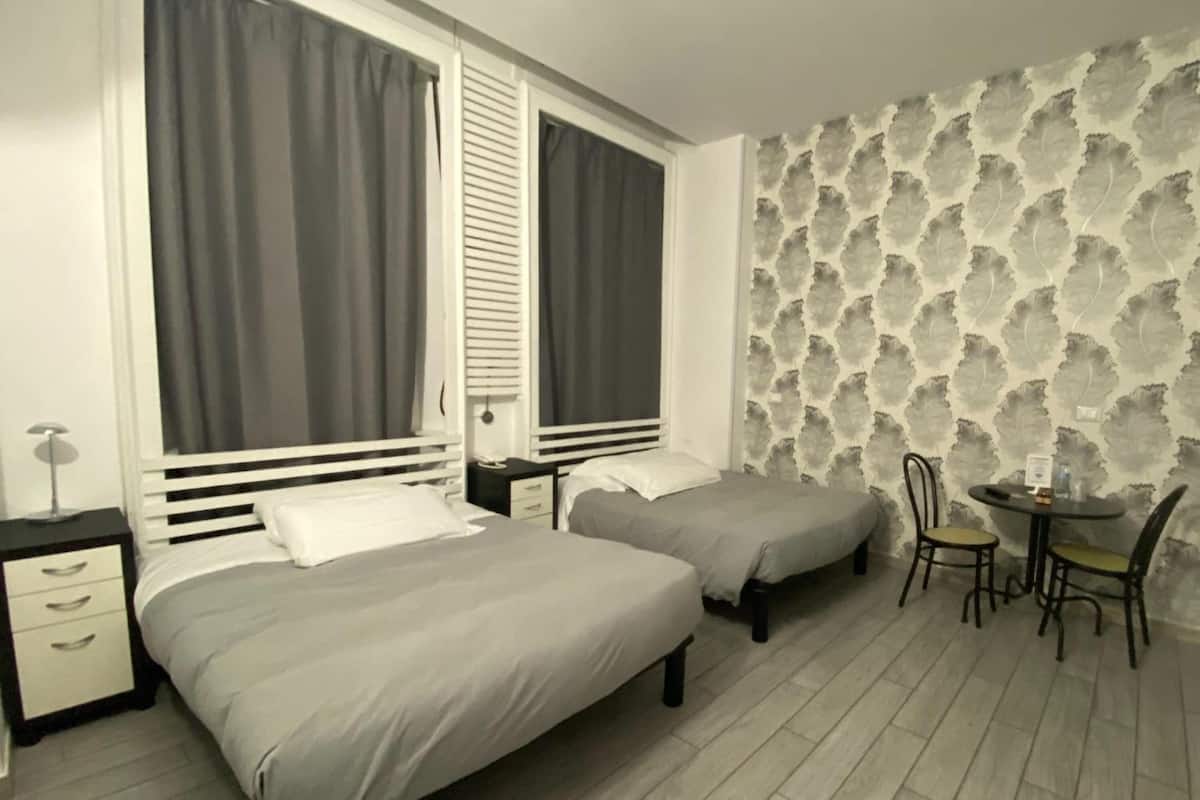 Una habitación con dos camas, una mesita con sillas y un papel tapiz estampado.