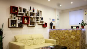 A hotel lobby with a beige sofa, a coffee table with magazines, and a reception desk with a stone backdrop. - Hotel RossoVino (Milan)
