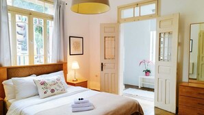 A bedroom with a bed, a bedside lamp, a framed picture on the wall, and a door leading to another room. - Eden Hotel (Haifa)