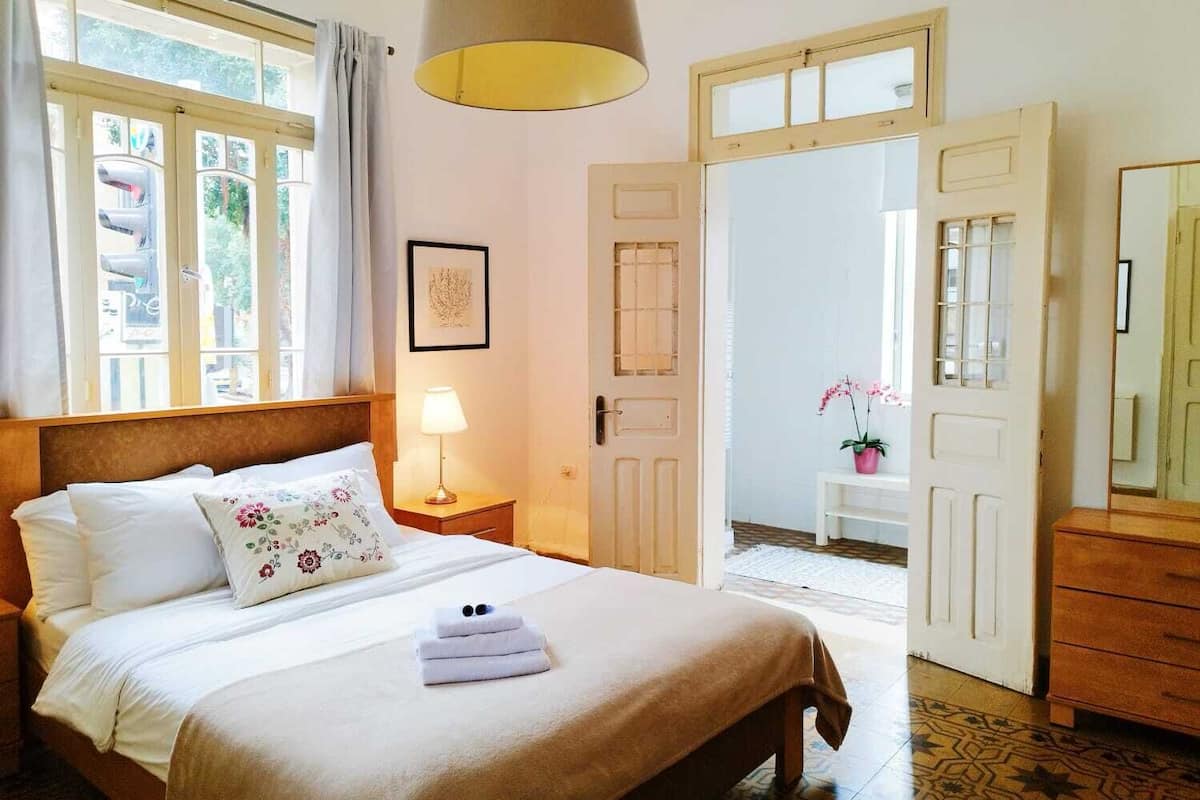 Ein Schlafzimmer mit einem Bett, einer Nachttischlampe, einem gerahmten Bild an der Wand und einer Tür zu einem anderen Raum.
