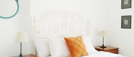 A neatly arranged bedroom with a bed, two bedside tables, a nightstand, a wall-mounted circular light, and a patterned rug.