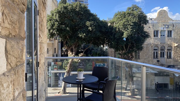 A balcony with a table and chairs, overlooking a cityscape with historic buildings and trees. - Eden Hotel (Haifa)