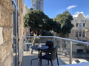 A balcony with a table and chairs, overlooking a cityscape with historic buildings and trees.