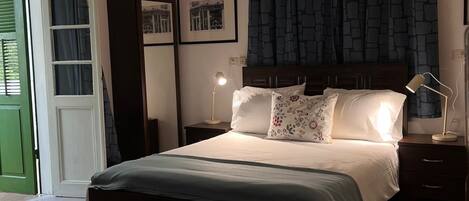 Un dormitorio con cama, mesitas de noche, escritorio, silla, armario y ventana con cortinas.