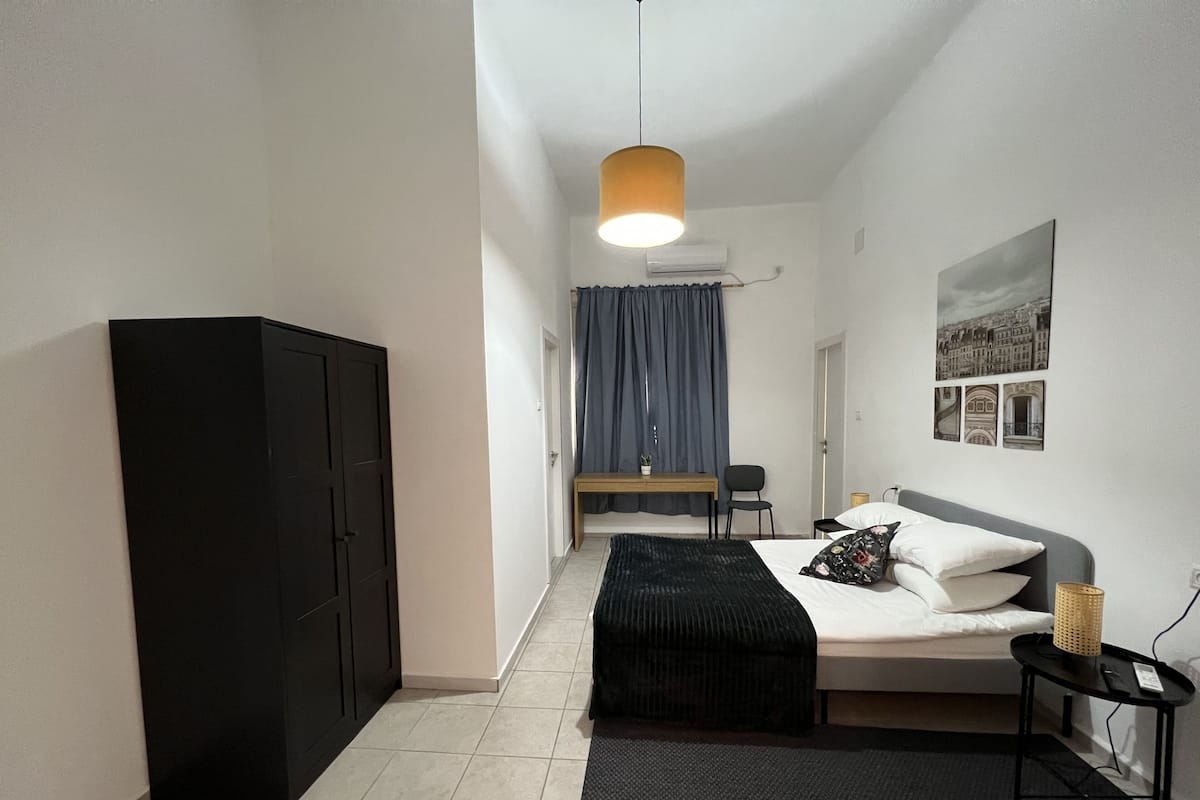 Ein Schlafzimmer mit einem Bett, einem Schreibtisch, einem Stuhl, einem Kleiderschrank und einer Pendelleuchte.