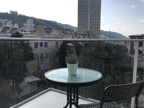 A balcony with a glass table and chairs, a potted plant, and a view of a cityscape with buildings and hills.