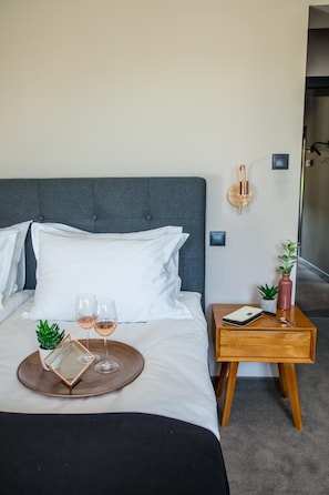 A neatly made bed with white linens, a bedside table with a book, a vase, and a small plant. There are two wine glasses on a tray. - Reverence (Varna)