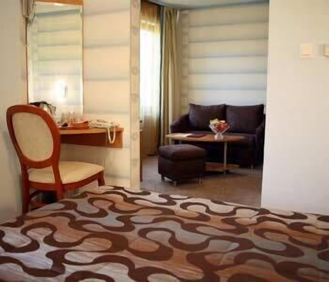 A hotel room with a bed, a desk, a chair, a sofa, and a small table with a vase of flowers.