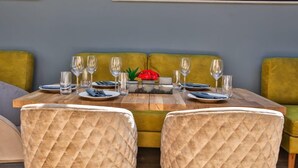 A dining area with a wooden table set for four, surrounded by two green upholstered sofas and two quilted chairs.