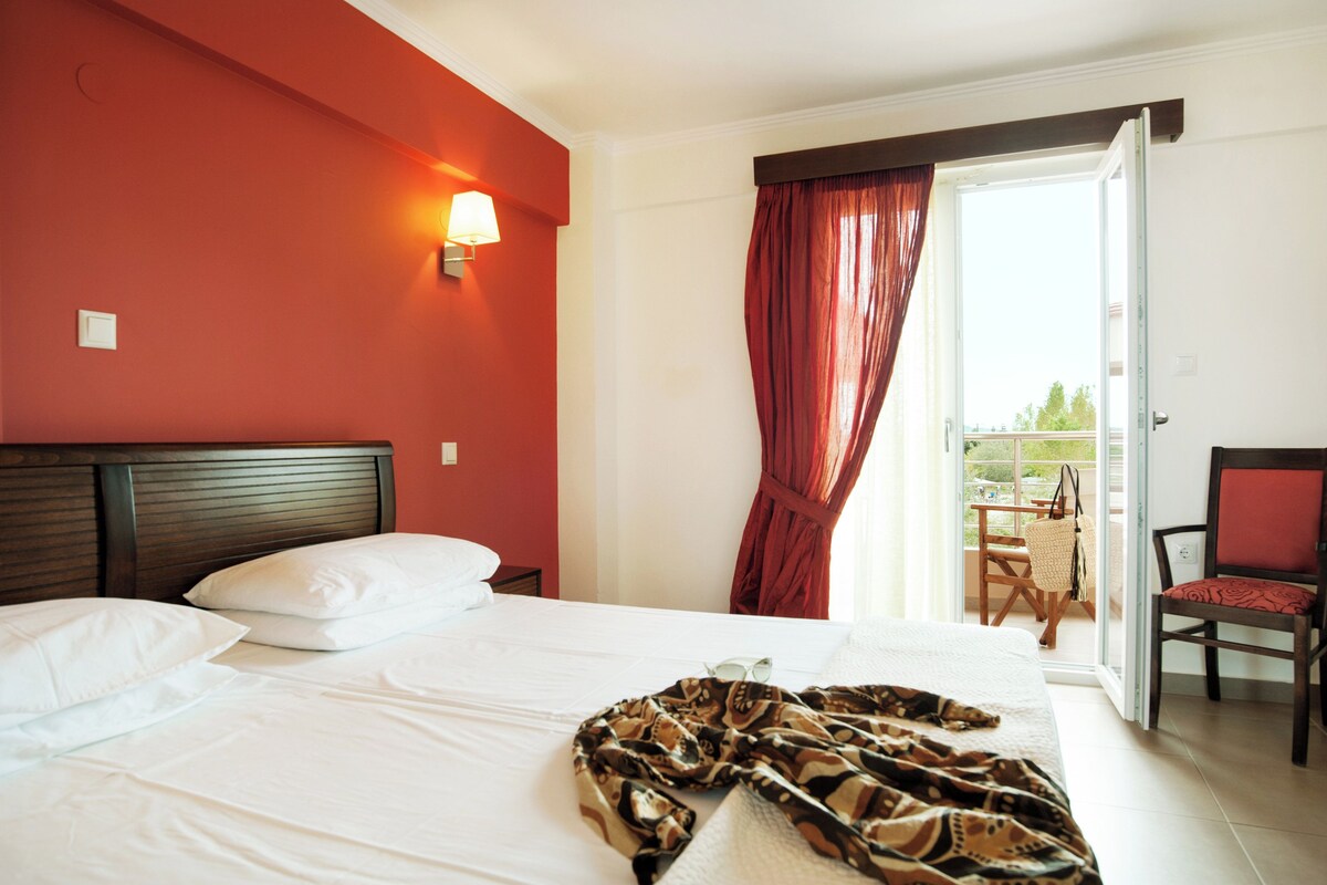 A hotel room with a bed, a nightstand, a lamp, a chair, and a view of the outdoors.