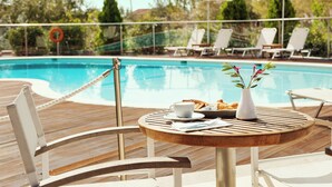 Zona de comedor junto a la piscina con mesa, sillas y vistas al agua.