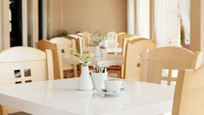 Un comedor con una mesa blanca, sillas, un florero con planta y una taza de café.