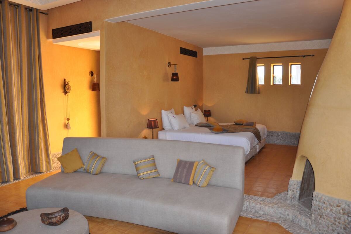 A hotel room with a sofa, a bed, a small table, and a stone fireplace.