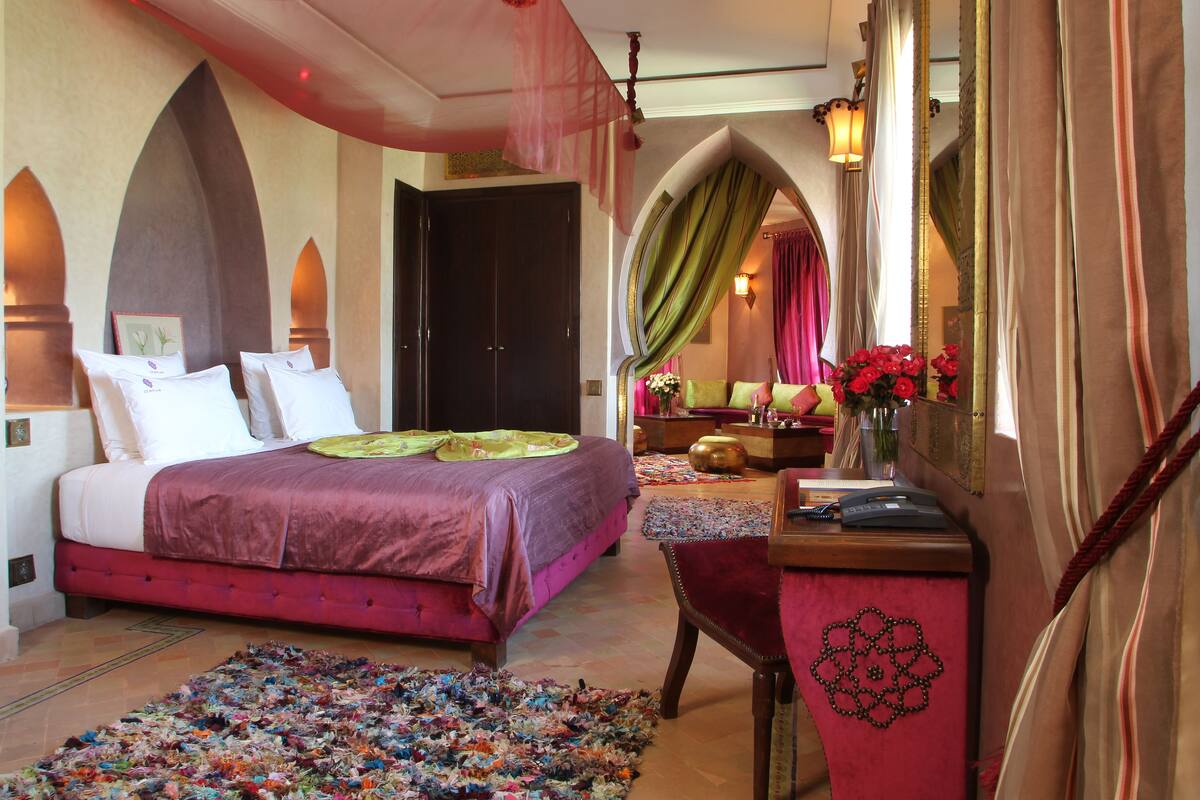 A bedroom with a large bed, a desk, and a mirror.