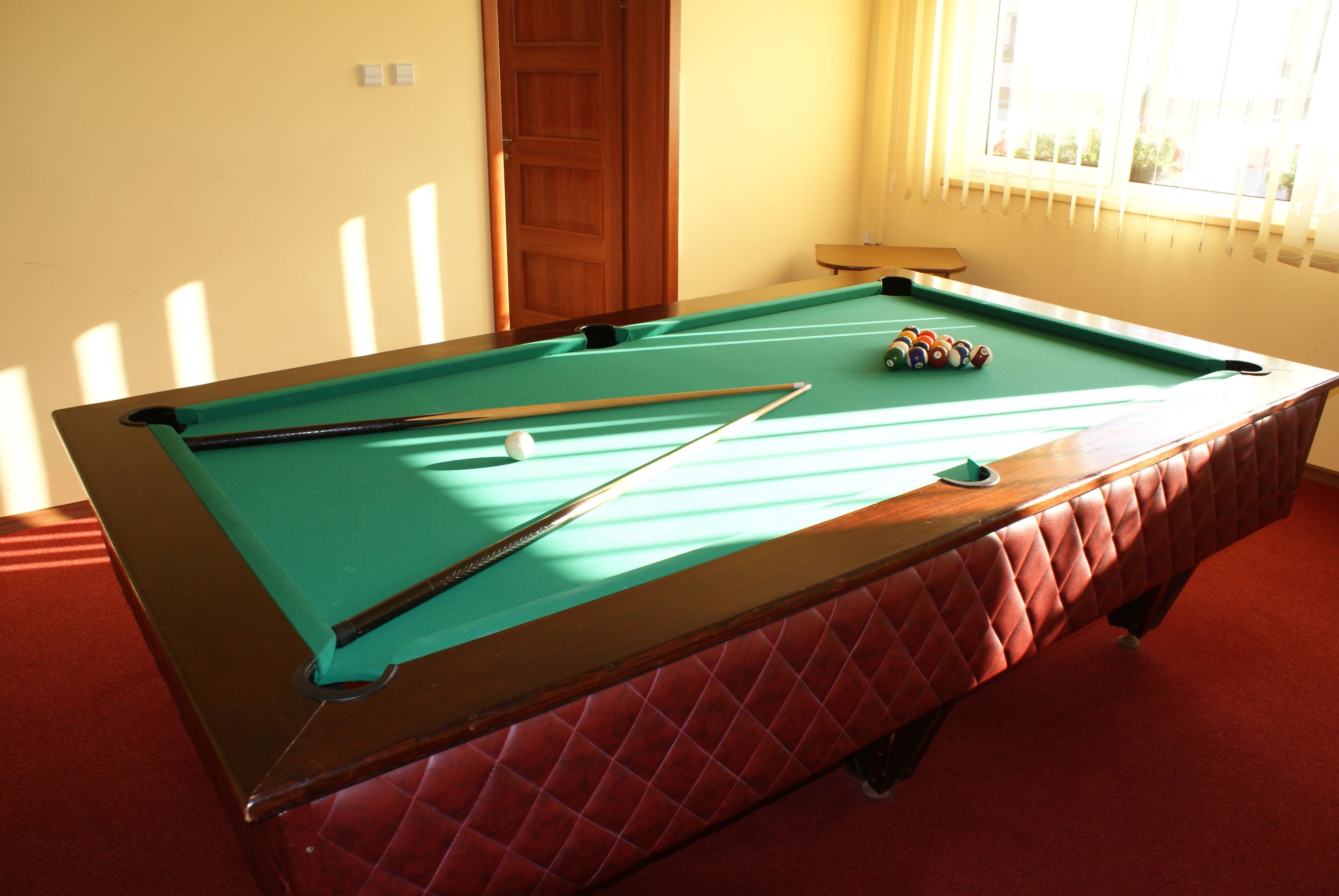 A pool table with balls and cues, a wooden door, and a window with blinds.