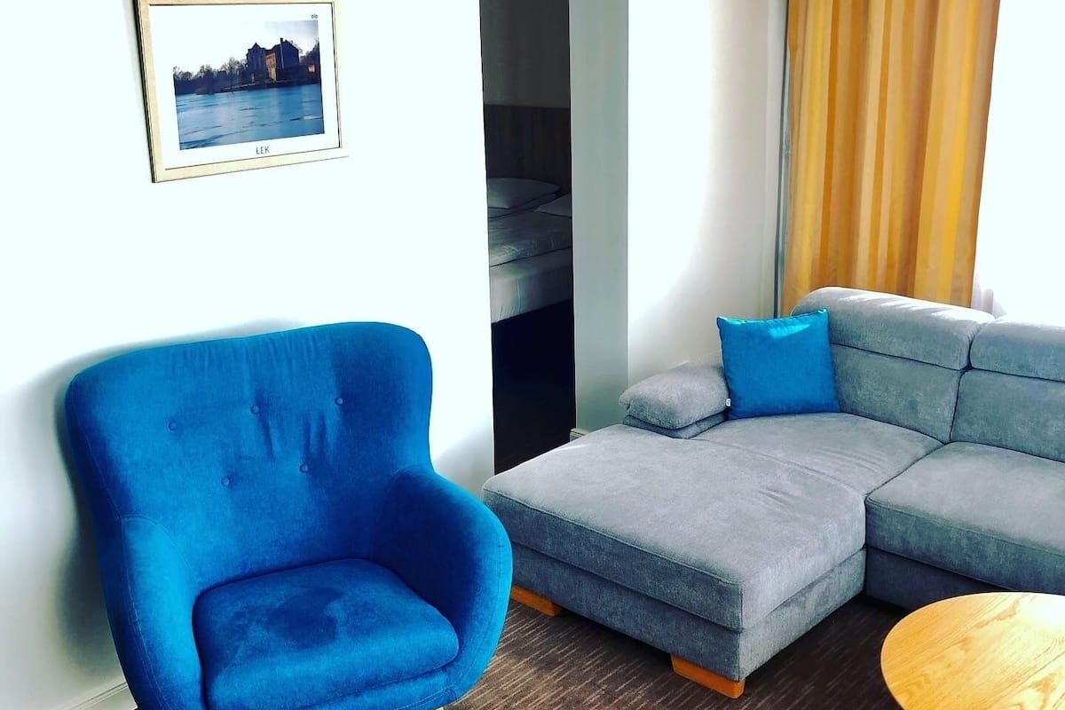 A modern living room with a blue armchair, a grey sectional sofa, and a small wooden table.