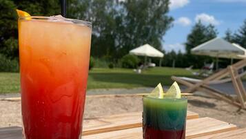 Two drinks on a wooden table outdoors with a grassy area and umbrellas in the background.