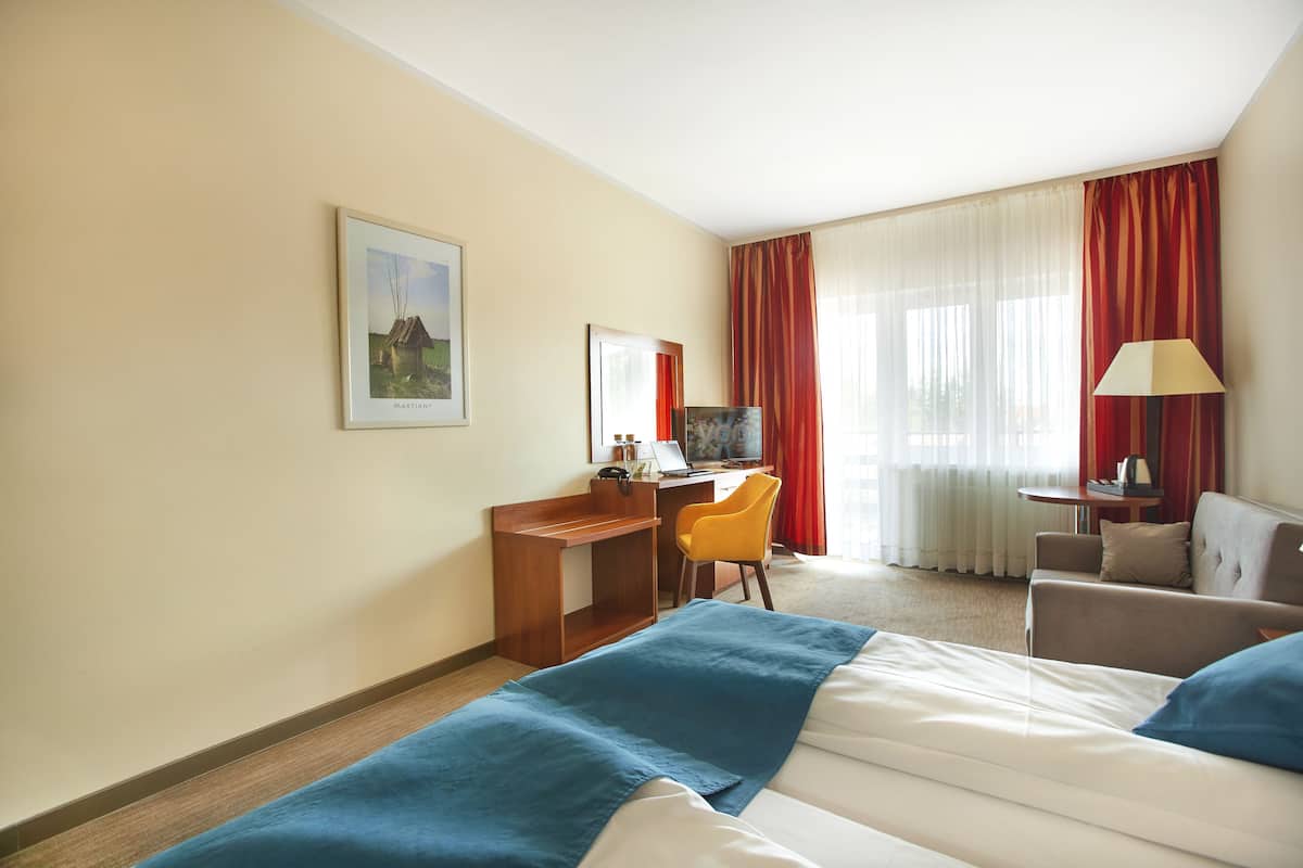 A hotel room with two beds, a desk, a chair, a sofa, and a window with curtains.