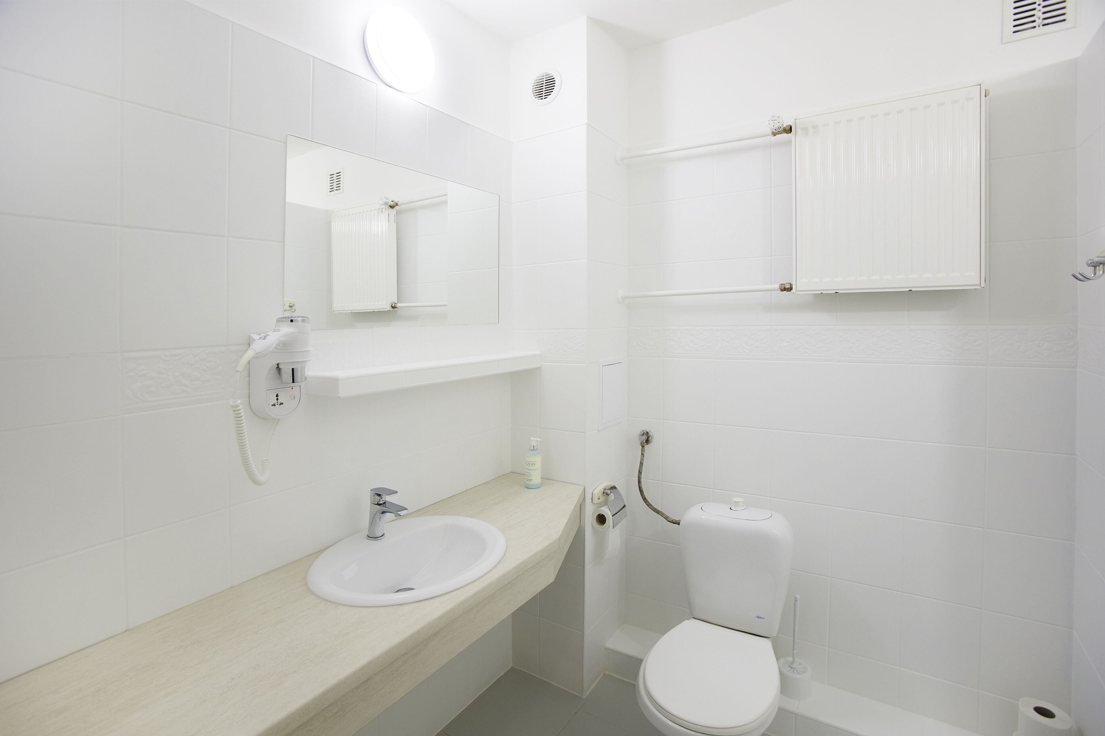 Un baño con lavamanos blanco, espejo, inodoro y toallero.