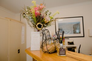 A wooden table with a wireframe vase containing flowers and a bottle of diffuser oil.