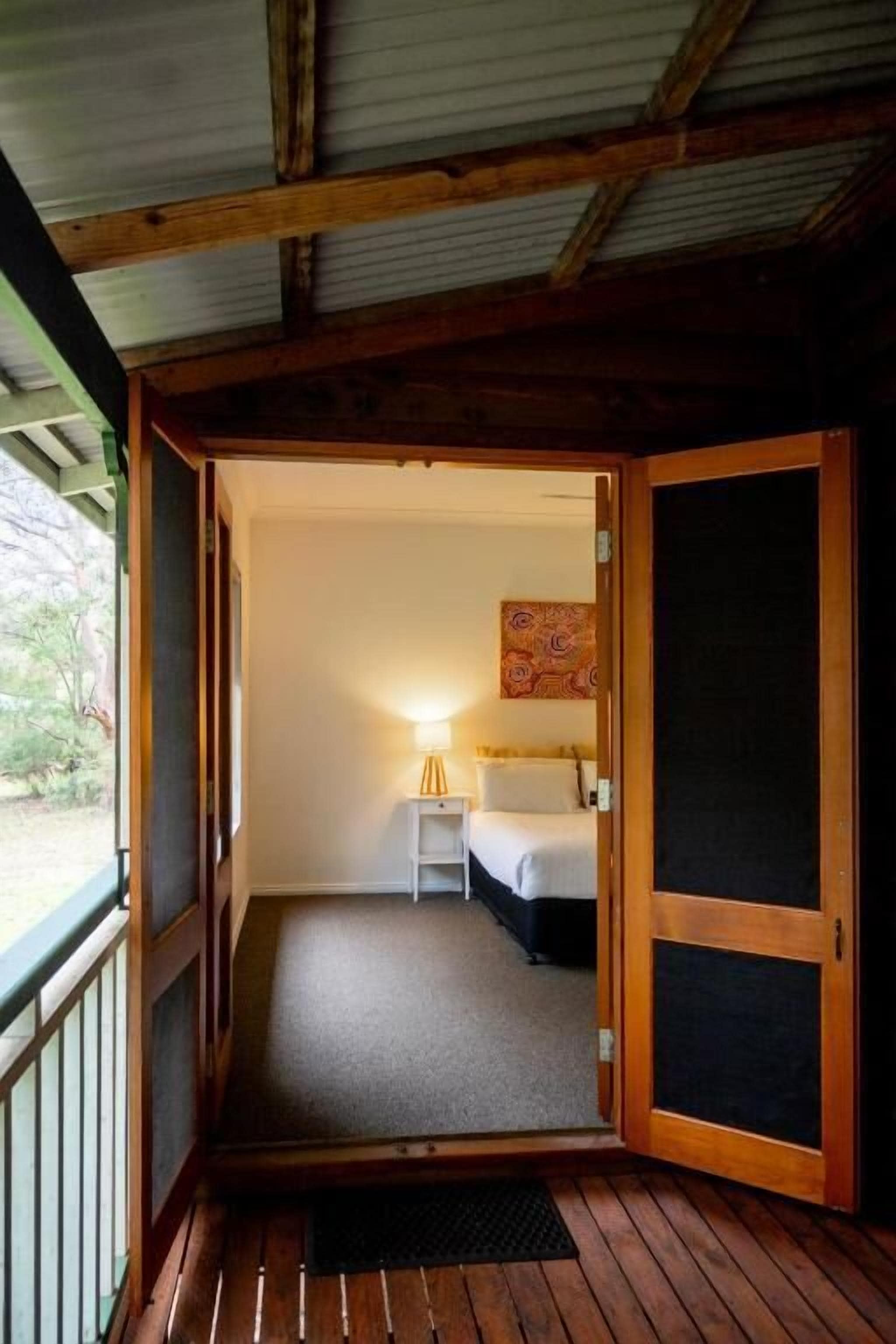 Une cabane en bois avec un balcon, un lit, une lampe de chevet et un tableau accroché au mur.