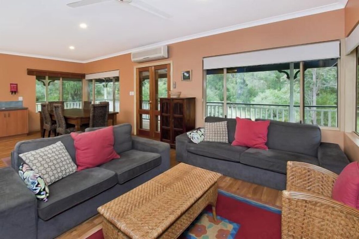 A living room with two grey sofas, a wicker bench, and a dining area with a table and chairs.
