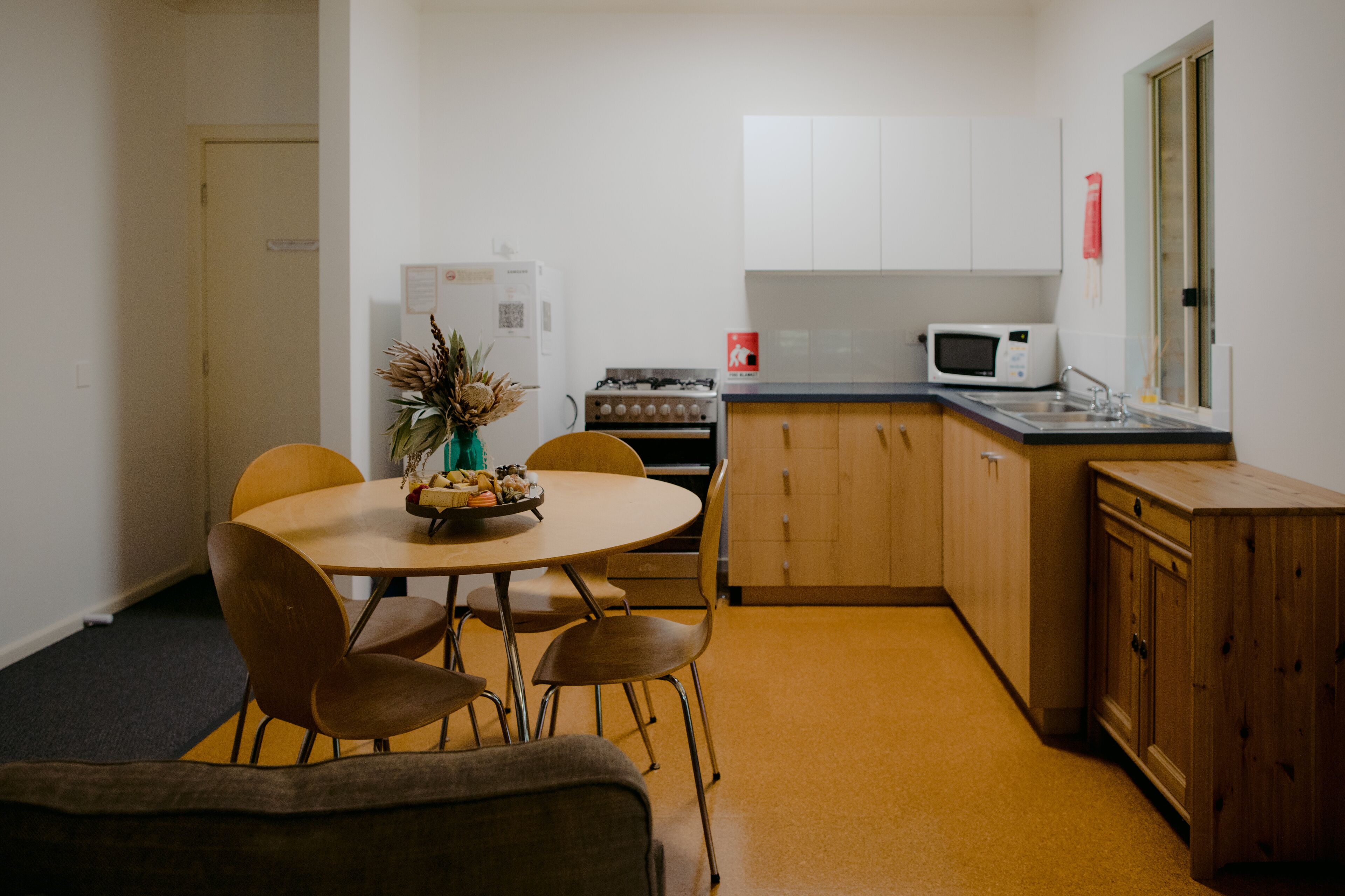 A compact kitchen with a dining table, chairs, a refrigerator, stove, microwave, and wooden cabinets.