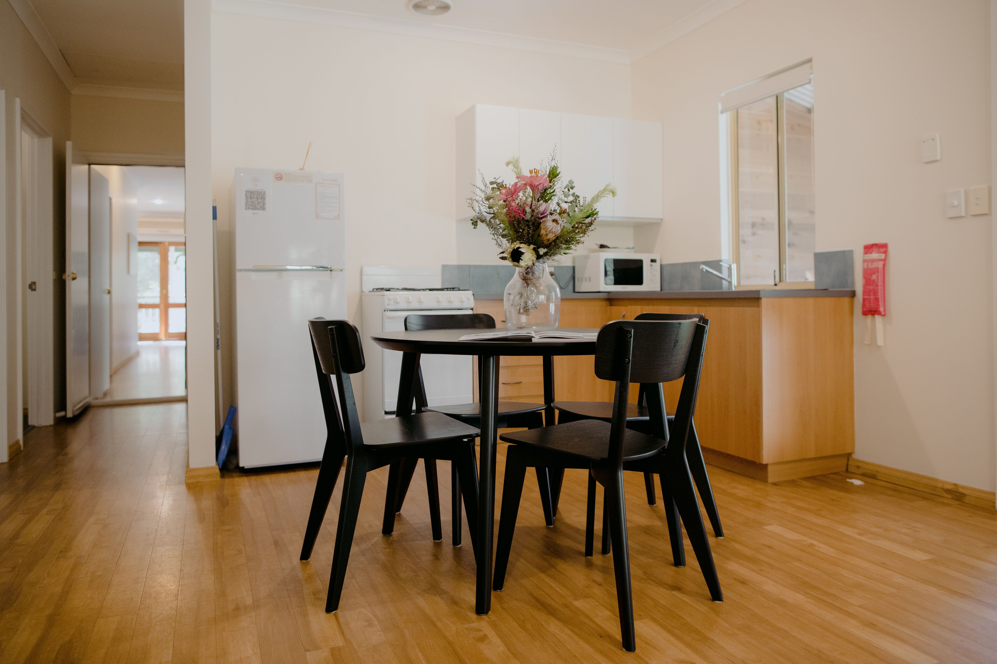 Une cuisine moderne avec un coin repas, comprenant un réfrigérateur, un four à micro-ondes et un vase rempli de fleurs posé sur le plan de travail.