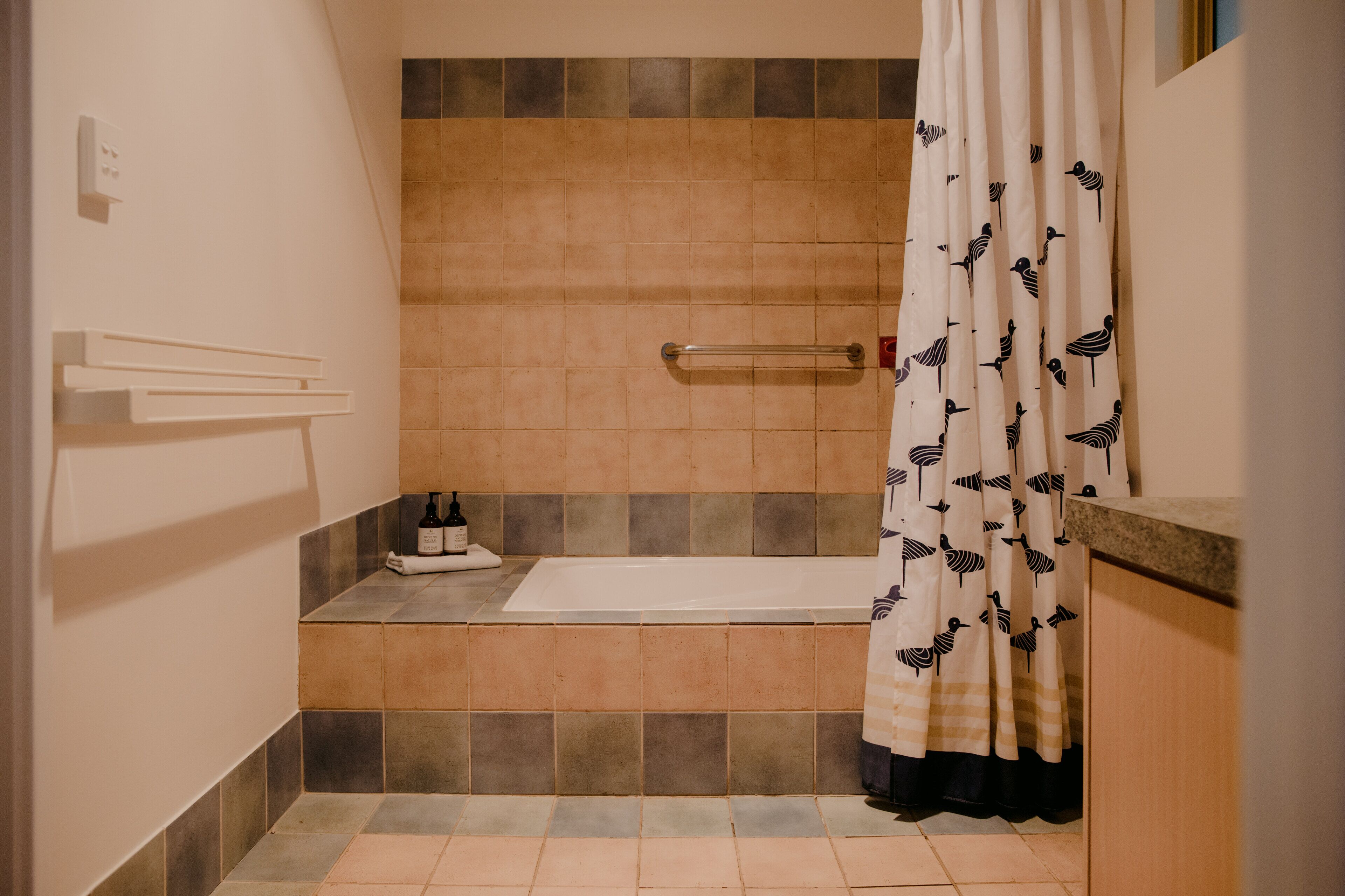 Un baño con bañera, toallero y cortina de ducha con estampado de aves.
