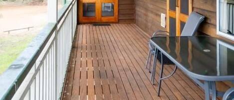 A wooden deck with a glass table and chairs, a door with a glass panel, and a view of the outdoors.