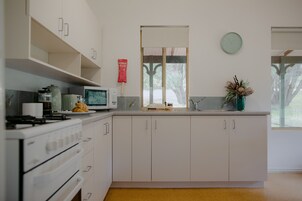 Cocina moderna con armarios blancos, microondas, estufa y ventana con vista a árboles.